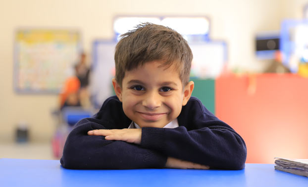 A young smiling Deaf child in the classroom